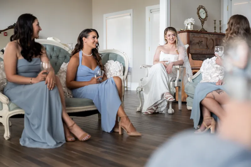 Bridesmaids in blue dresses sit together at White Room while Skye prepares in a nearby room.