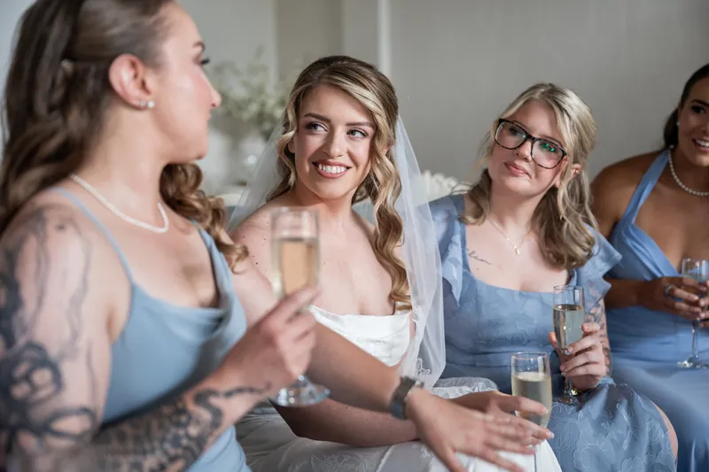 Skye smiles with bridesmaids in coordinating blue dresses holding champagne flutes during getting ready.