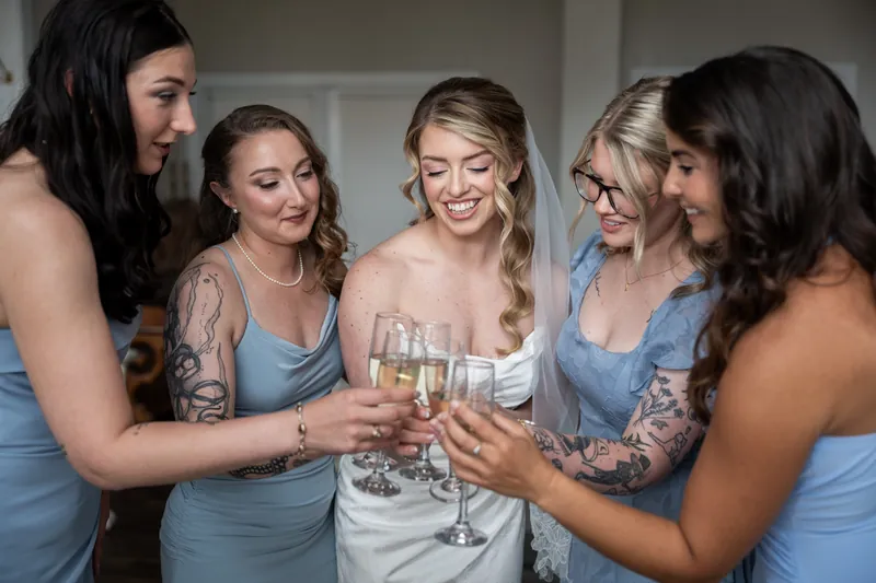 Five bridesmaids in light blue dresses clink champagne glasses around Skye in her white wedding gown.