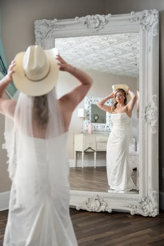 A guest admires Skye's reflection in an ornate white-framed mirror as she adjusts her veil.
