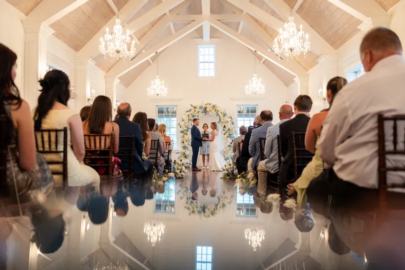 Wedding guests seated in the White Room's ceremony space with reflective flooring and chandeliers.