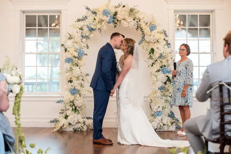 Elliot kisses Skye under the floral arch as guests watch during their White Room ceremony.