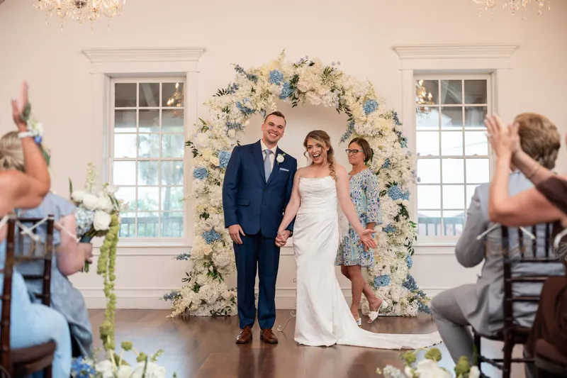 Skye and Elliot stand together under the bloom-decorated arch after being pronounced married at White Room.