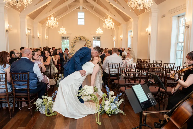 Elliot dips Skye during their first dance at The White Room, with guests watching from wooden chairs beneath crystal chandeliers.