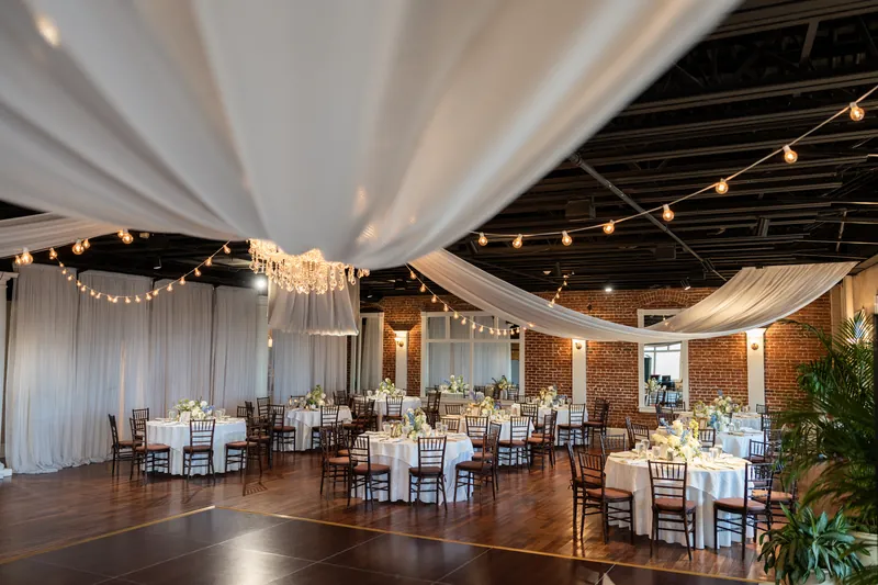 The White Room reception space features draped white fabric, string lights, and round tables set for dinner.