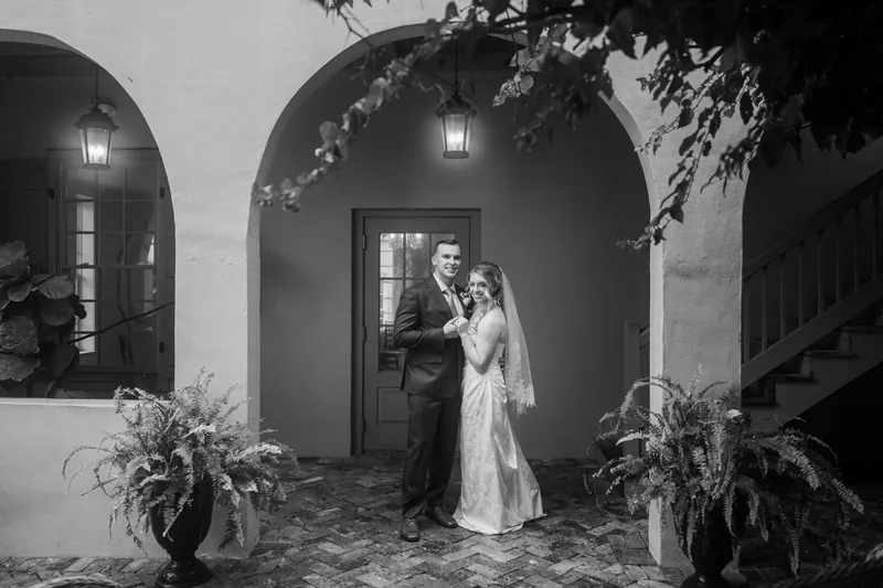 Skye and Elliot stand together under a brick archway at the White Room's entrance in this black and white portrait.