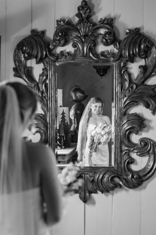 Ornate black mirror reflects Skye in her beaded gown standing in an elegant hallway during preparations.