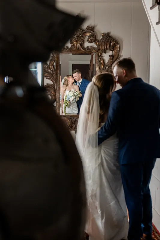 Elliot in a navy suit stands with Skye at the altar as guests watch during their White Room ceremony.