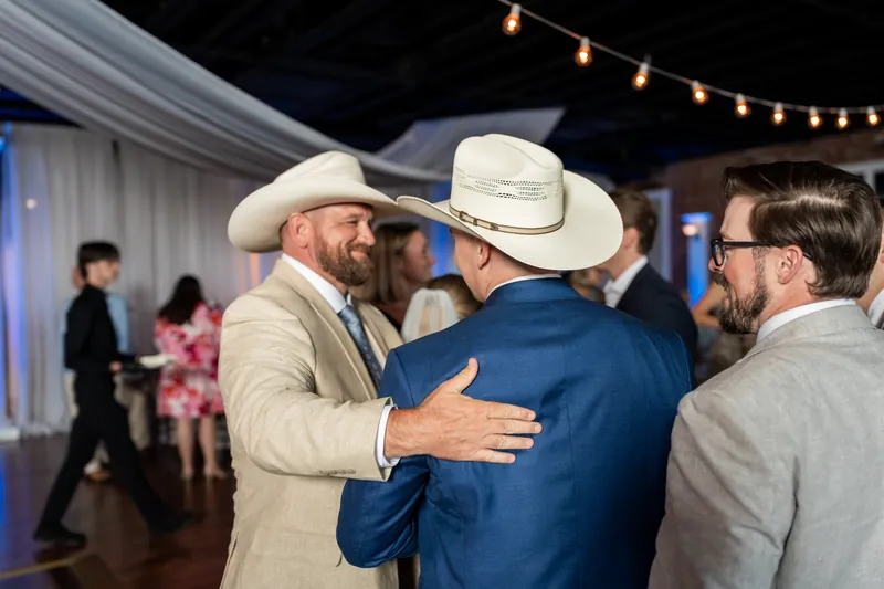 Guests in cowboy hats embrace and celebrate at Skye and Elliot's reception.