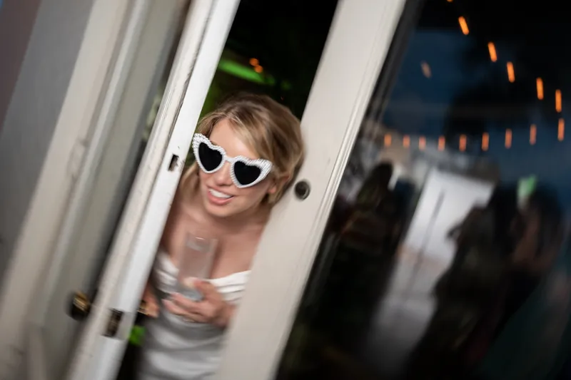 Guest peers through a doorway wearing heart-shaped sunglasses at the White Room reception.
