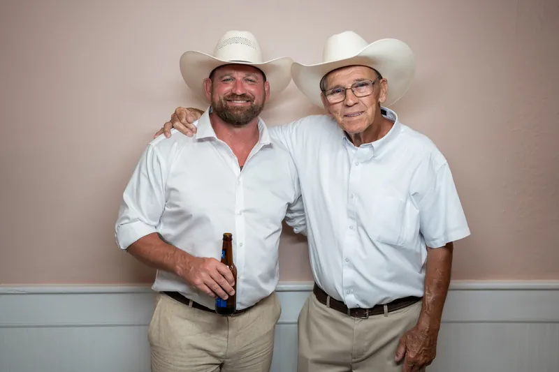 Two men wearing white cowboy hats and light blue shirts pose together at the White Room.