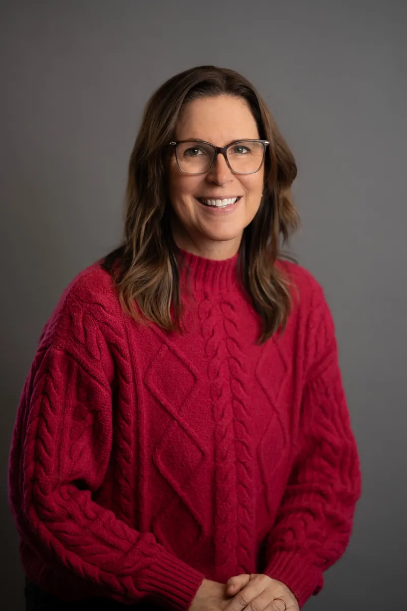 Professional headshot of woman in red cable-knit sweater with glasses