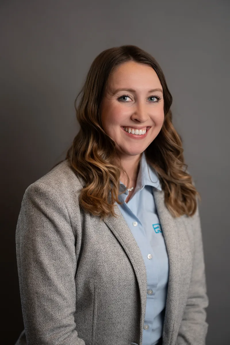 Professional headshot of woman in gray blazer over light blue shirt