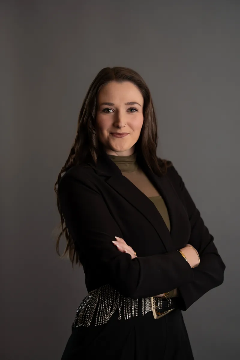 Professional headshot of woman in black blazer with sparkly fringe belt