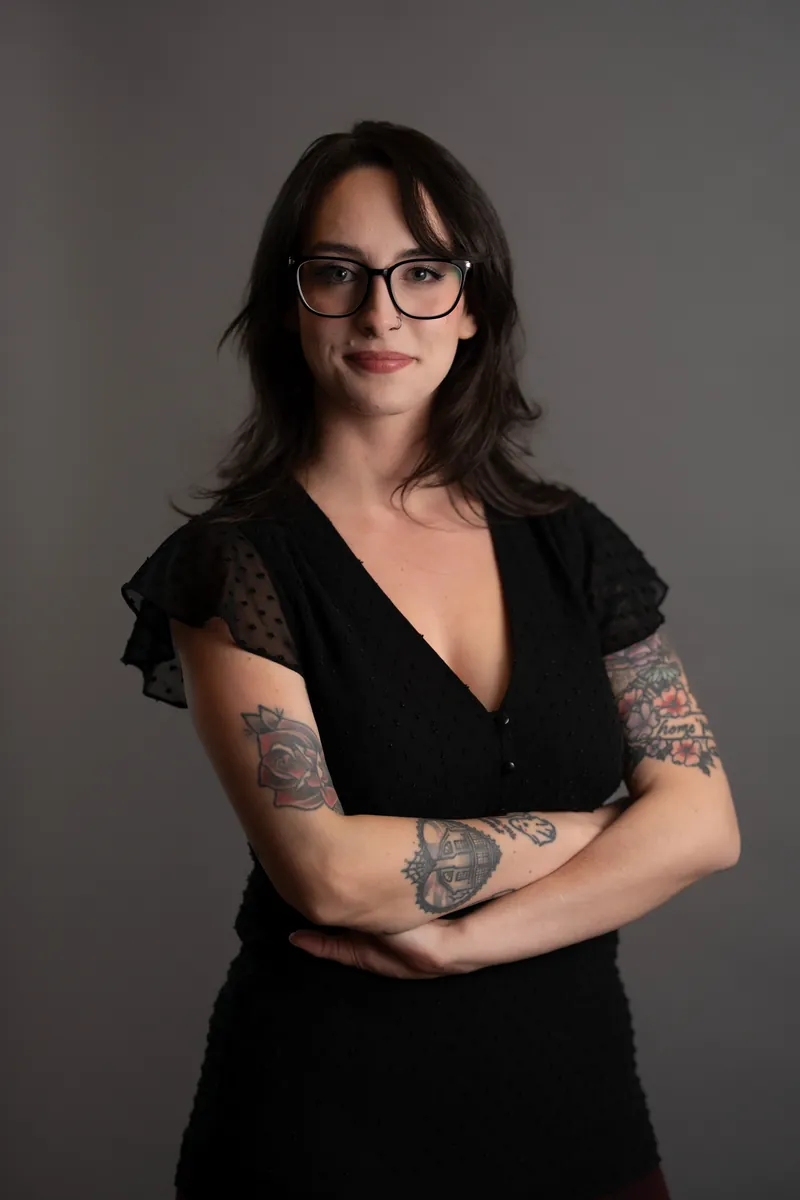 Professional headshot of woman in black dress with tattoos