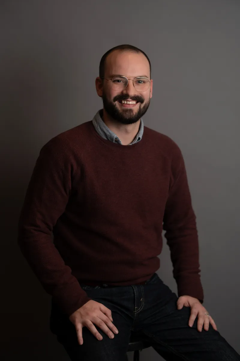 Professional headshot of man in burgundy sweater with glasses