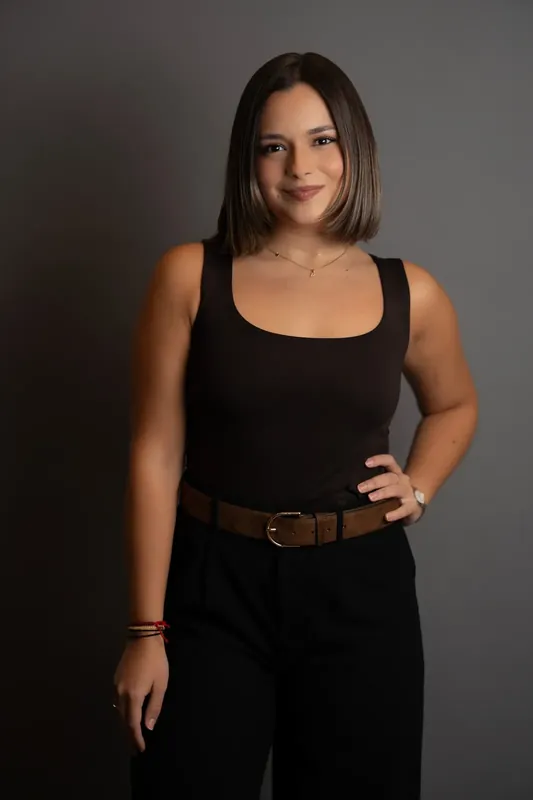 Person in a sleeveless black tank top with a brown belt poses with hand on hip.