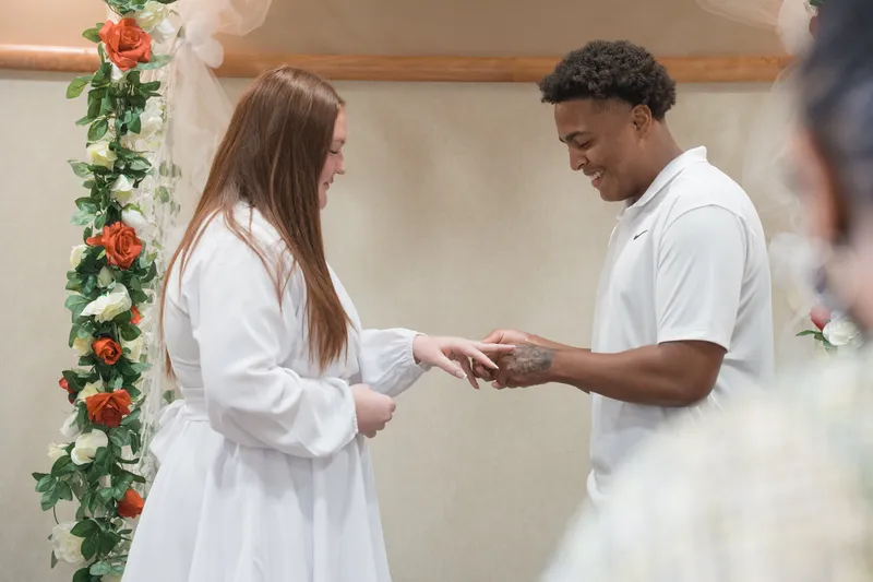 A bride and groom exchange rings during their intimate courthouse elopement ceremony, standing beneath a beautiful floral arch.