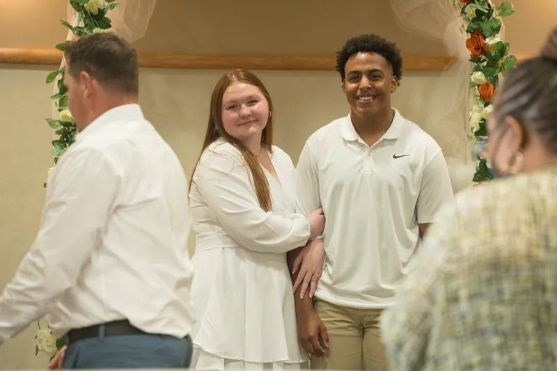 A joyful couple stands together during their intimate courthouse elopement ceremony, with the bride in a white robe and groom in a polo shirt.