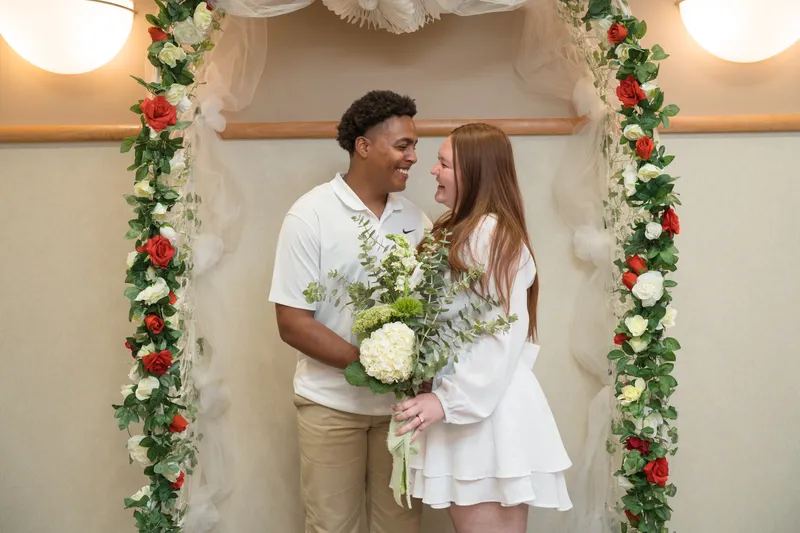 A newlywed couple shares an intimate moment under a floral arch after their courthouse elopement ceremony, gazing lovingly at each other.