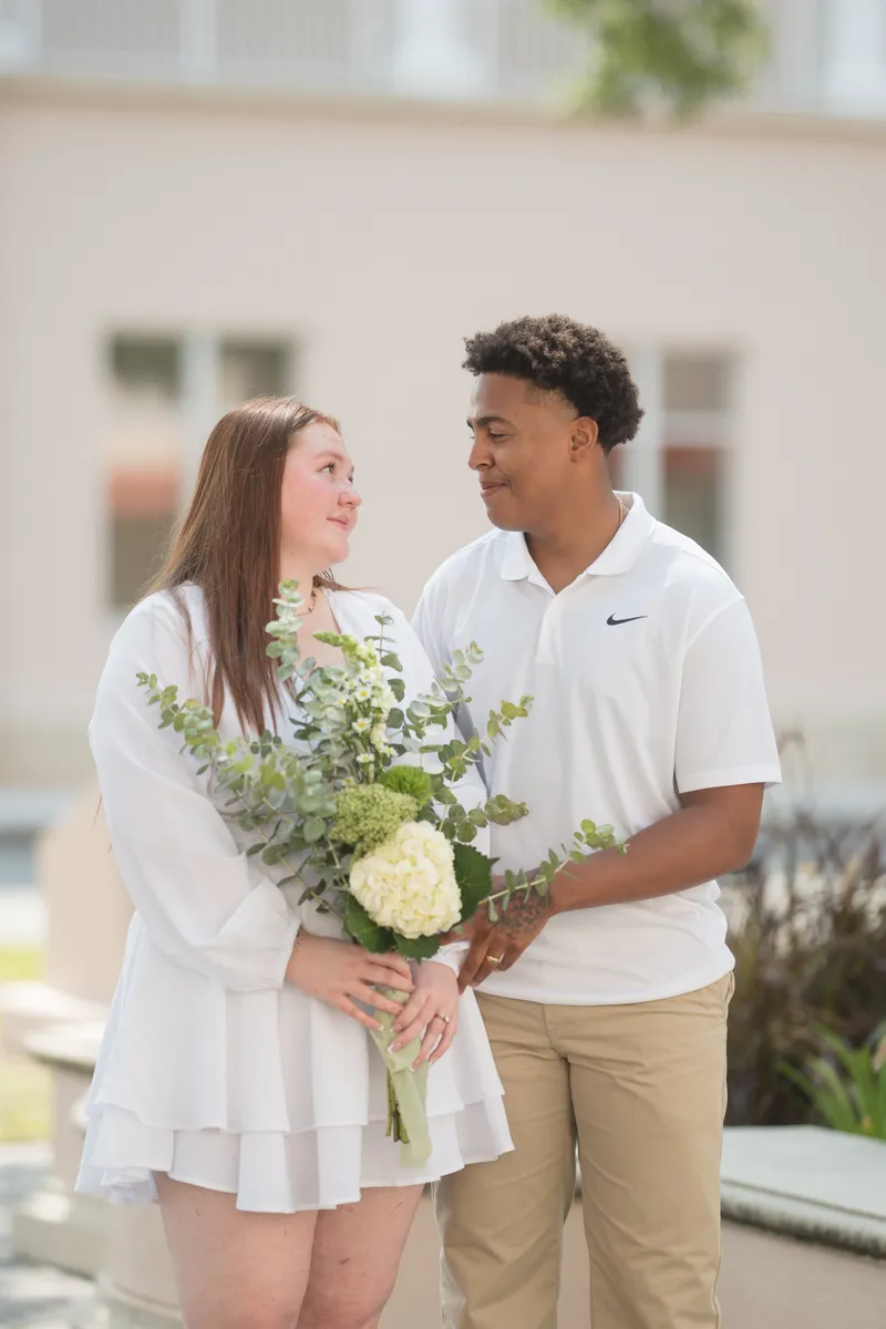 A happy couple shares an intimate moment after their courthouse elopement, with the bride holding a beautiful bouquet of white flowers and greenery.