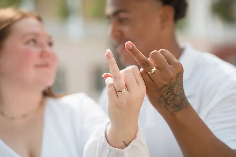 A newly married couple playfully shows off their matching wedding rings, with hands pressed together in celebration.