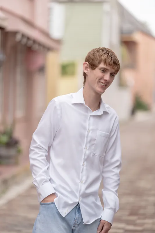 Spencer smiles with his hands in his pockets, wearing a white long-sleeve shirt and jeans on a brick pathway in Downtown St