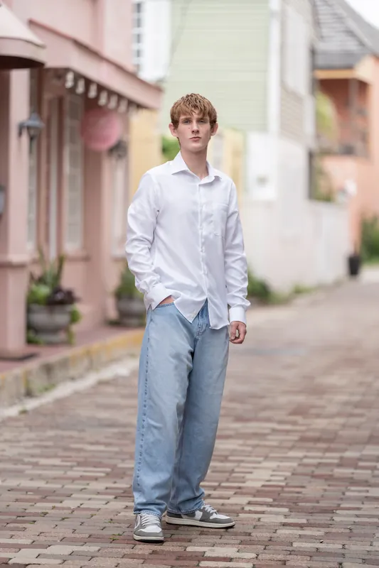 Spencer walks down a brick street in Downtown St Augustine wearing jeans, a white shirt, and sneakers, with historic pastel
