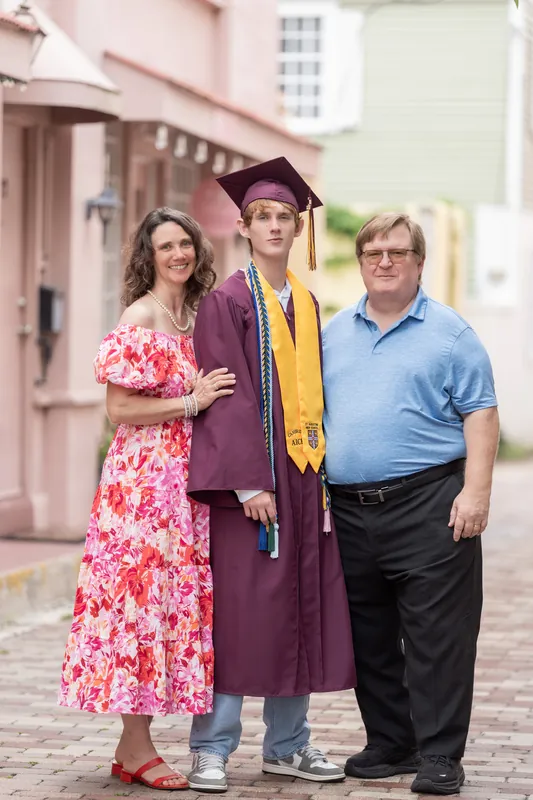Spencer poses between two family members on a shaded brick street lined with historic architecture.