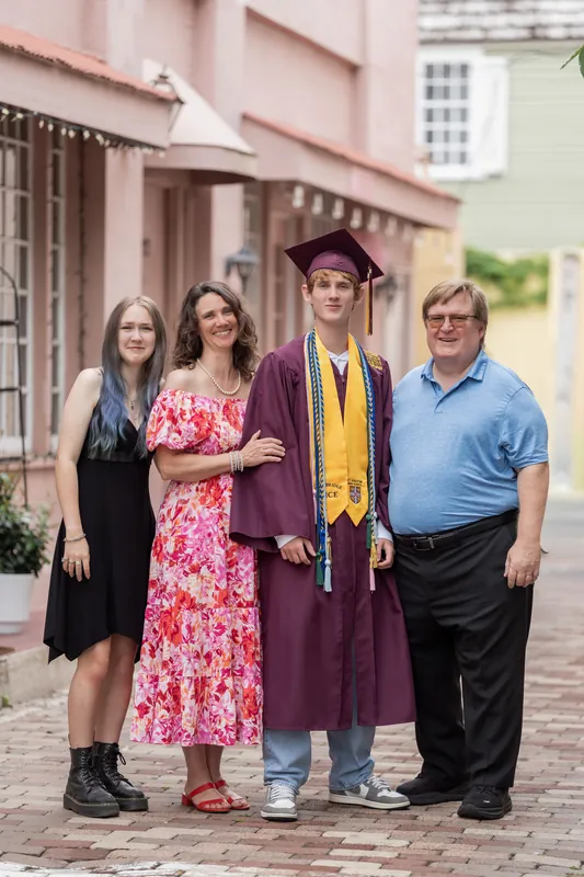 Four family members stand together for a portrait on the brick pedestrian street, with Spencer centered in his graduation