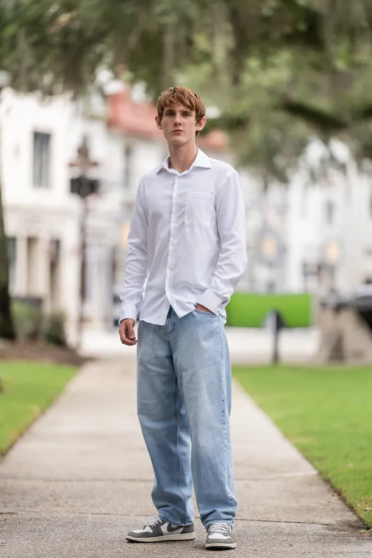 Spencer strolls past historic buildings and green grass, dressed casually in a white shirt and blue jeans.