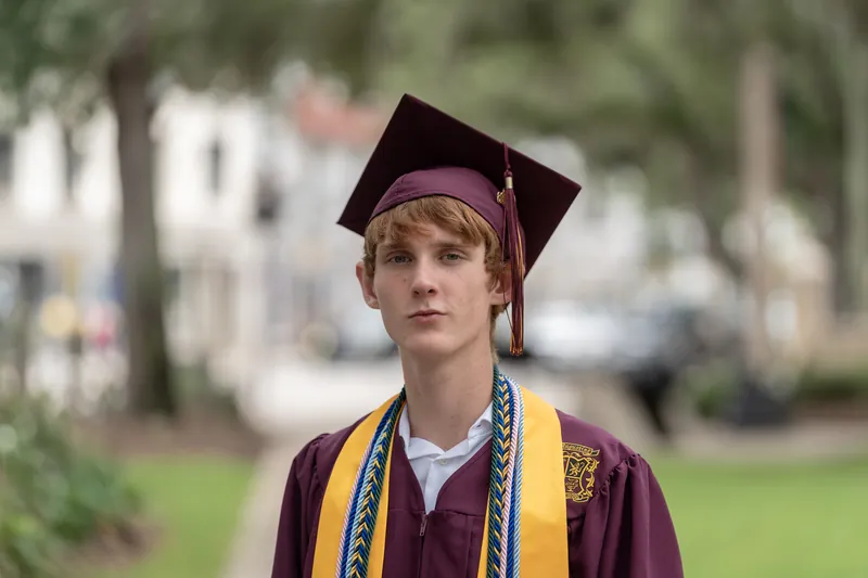 Spencer in cap and gown with gold honor cords stands in Downtown St Augustine's historic district.