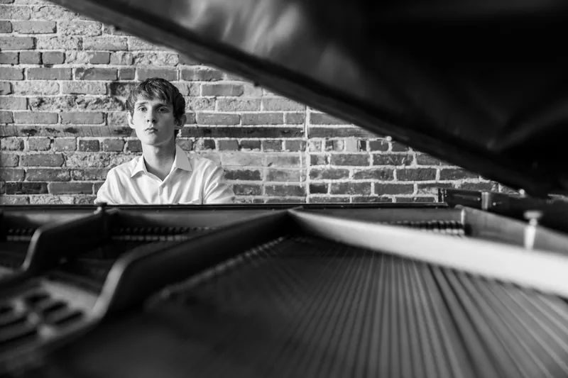 Black and white portrait of Spencer seated at a piano with brick wall behind him.