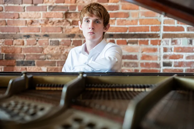 Spencer gazes thoughtfully over the piano keys with red brick visible in the background.