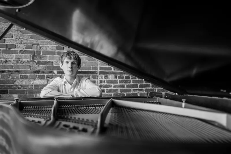 Black and white shot of Spencer seated at the piano, framed by the instrument's interior.