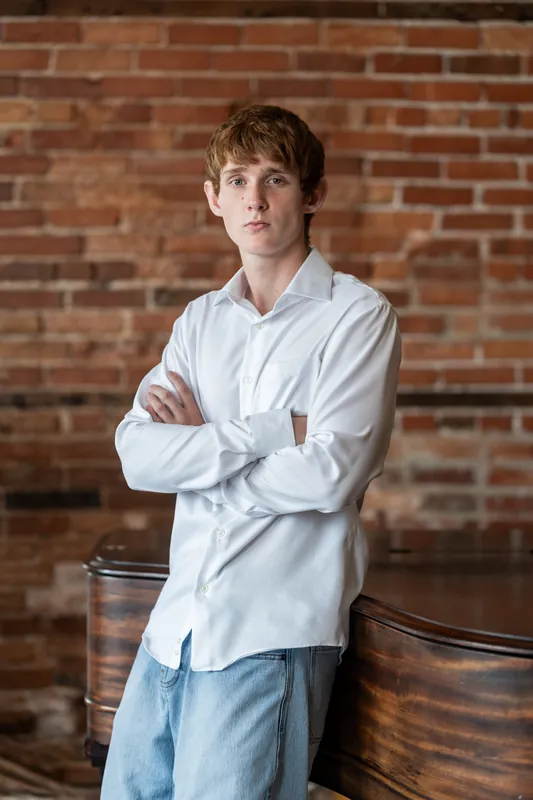 Spencer stands with arms crossed in a light blue shirt next to the grand piano.