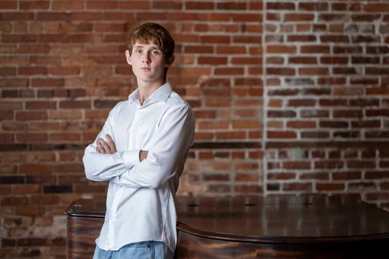 Spencer wears a light blue shirt with arms crossed, leaning casually against red brick in Downtown St Augustine.