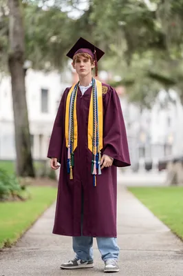 Graduate in maroon cap and gown on tree-lined path, St. Augustine family photographer