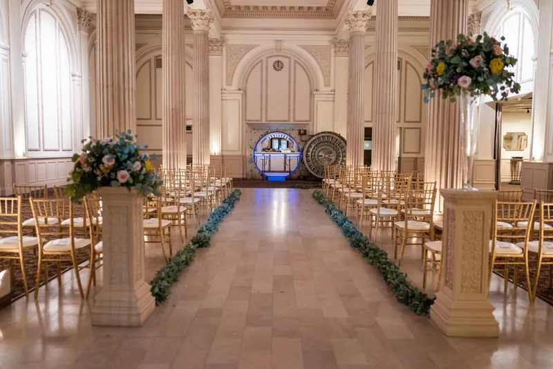 Ceremony aisle lined with greenery garland and tall floral arrangements leading to a blue-lit arch at The Treasury