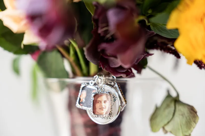 Silver locket charm hanging from the bouquet stem displays a photo pendant among yellow and purple flowers.