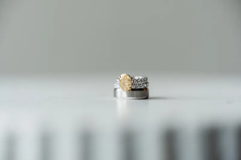 Gold and diamond engagement ring with matching diamond band rests on a neutral surface.