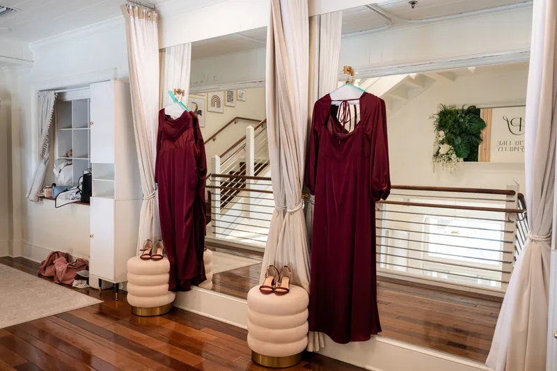 Two burgundy velvet robes displayed on mannequins in a bright room with wooden flooring and white railings.