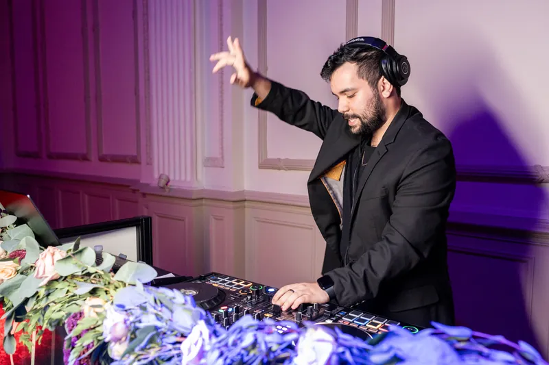 A DJ in a black suit gestures expressively while performing at the reception.