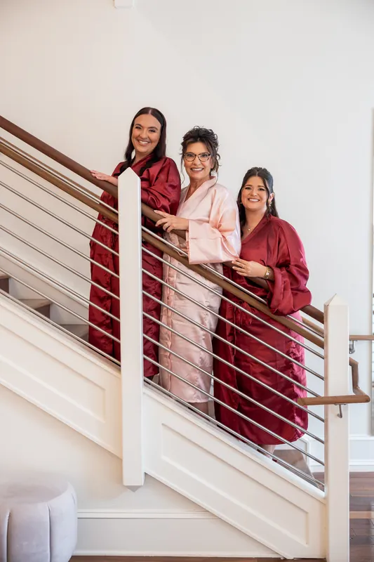 Three people in matching burgundy and pink robes stand together on a staircase with metal railings at The Plaza Suite.