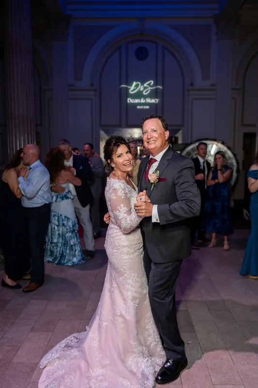 Stacy and Dean dance together in the grand hall as wedding guests watch nearby.