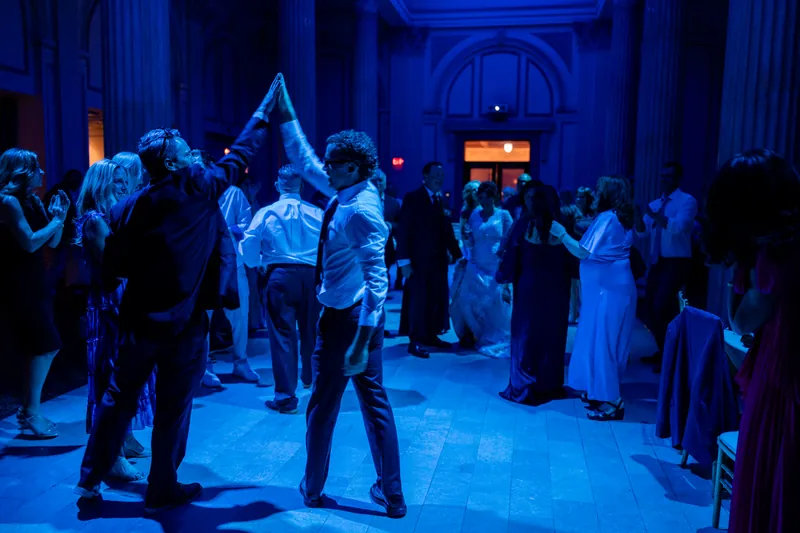 Guests mingle and dance across an illuminated blue floor under arched columns.
