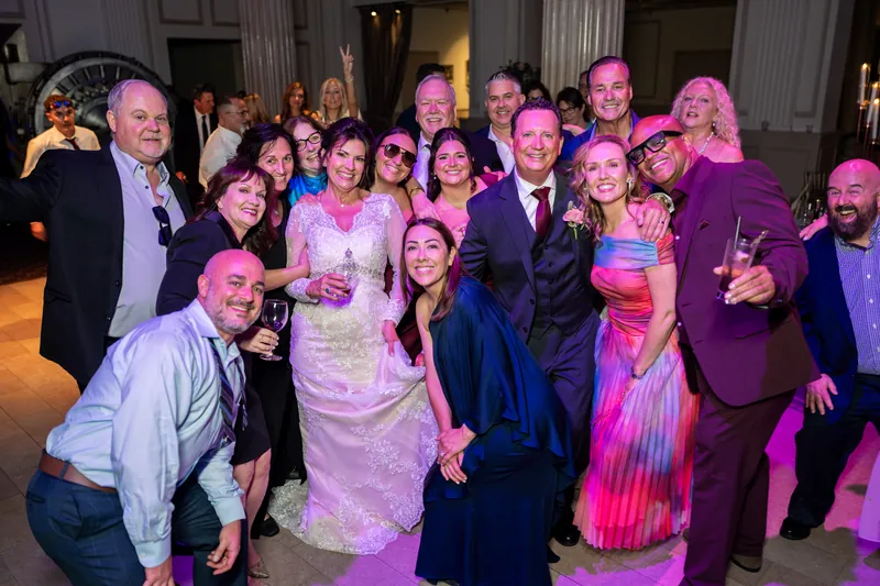 Stacy poses with a large group of friends and family members holding drinks and smiling.