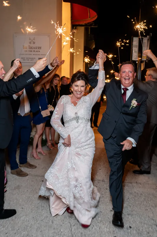 Stacy and Dean run through a sparkler tunnel as guests line both sides cheering.