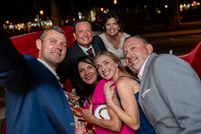 Six guests in formal attire smile together on a red seating area at The Treasury on the Plaza, with evening lights glowing
