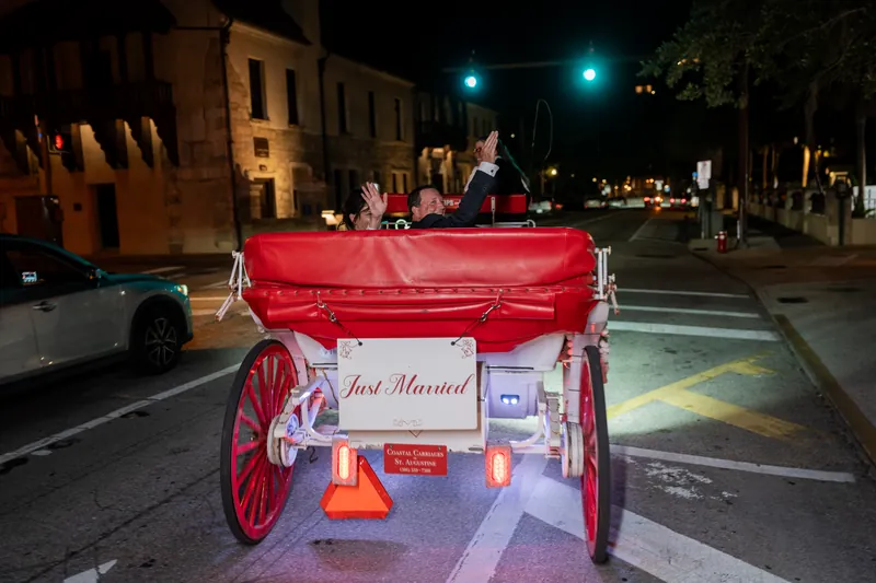 A red vintage getaway car decorated with "Just Married" sits parked on a historic street lined with colonial buildings